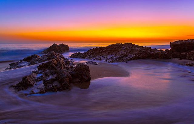A tranquil beach sunset with rocks and gentle waves, offering a serene coastal landscape for travel and relaxation.