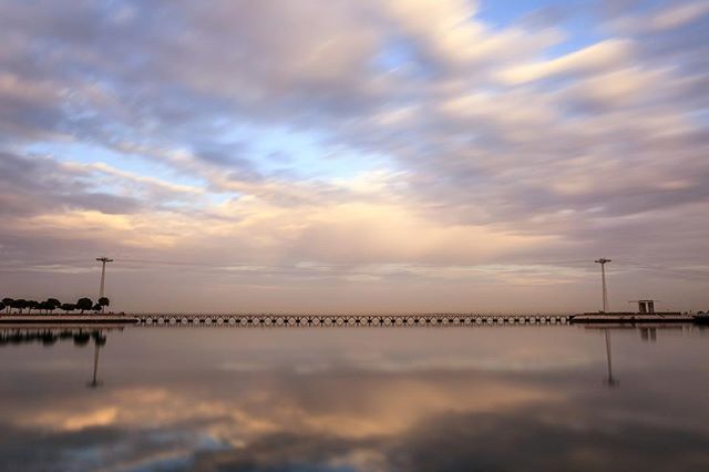 A long pier stretches across calm water under a pastel sky, offering a serene escape. 