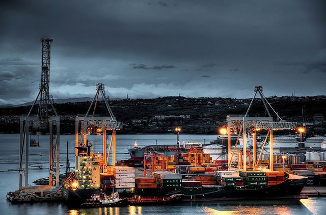Night view of a port with cranes and cargo ships loaded with containers in an industrial area.