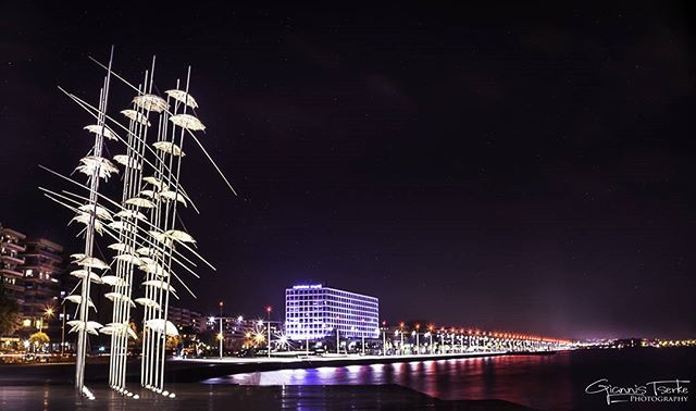 Night view of the illuminated umbrellas sculpture on the waterfront promenade in a city, creating a tranquil scene.