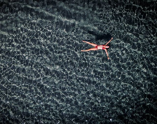 Aerial view of a woman in a red bikini floating in calm, clear water.