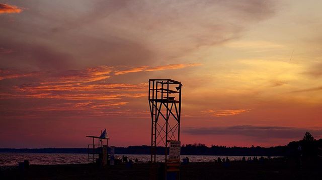 A scenic sunset over a beach with a lifeguard tower and people enjoying the tranquil evening atmosphere.
