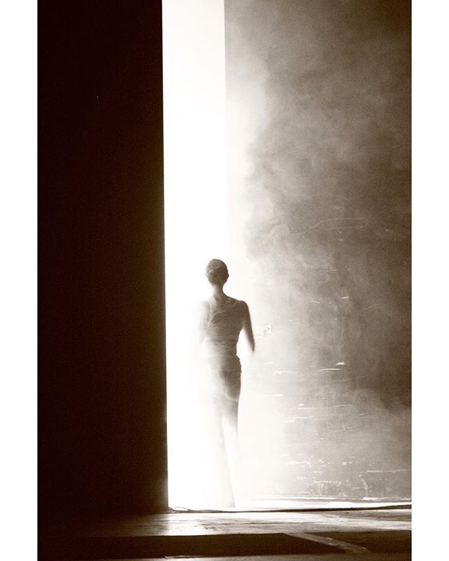 A silhouette of a woman walking into a brightly lit doorway, creating a sense of mystery and contemplation.