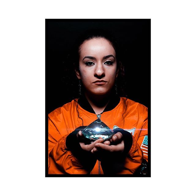 A woman in an orange jacket holds a diamond crystal in a studio setting.