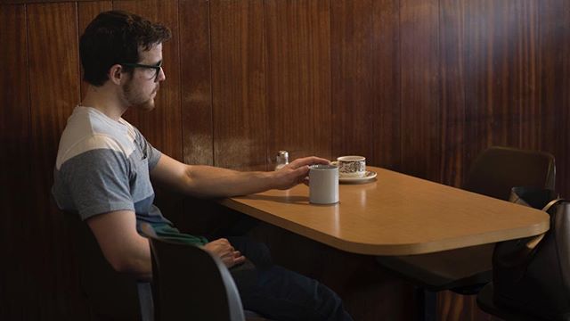 A man sits alone at a table in a cafe, enjoying a cup of coffee in a quiet moment.