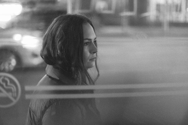 Black and white photo of a woman looking out into the night in an urban scene.