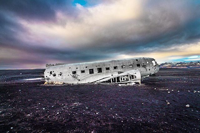 A desolate plane wreck sits on a black sand beach under a moody sky in Iceland.