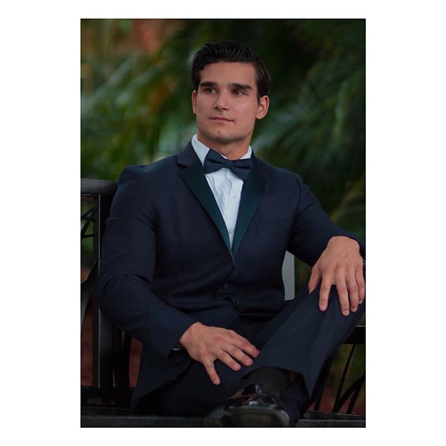 A handsome man in a suit and bow tie sits outdoors, exuding confidence and style.