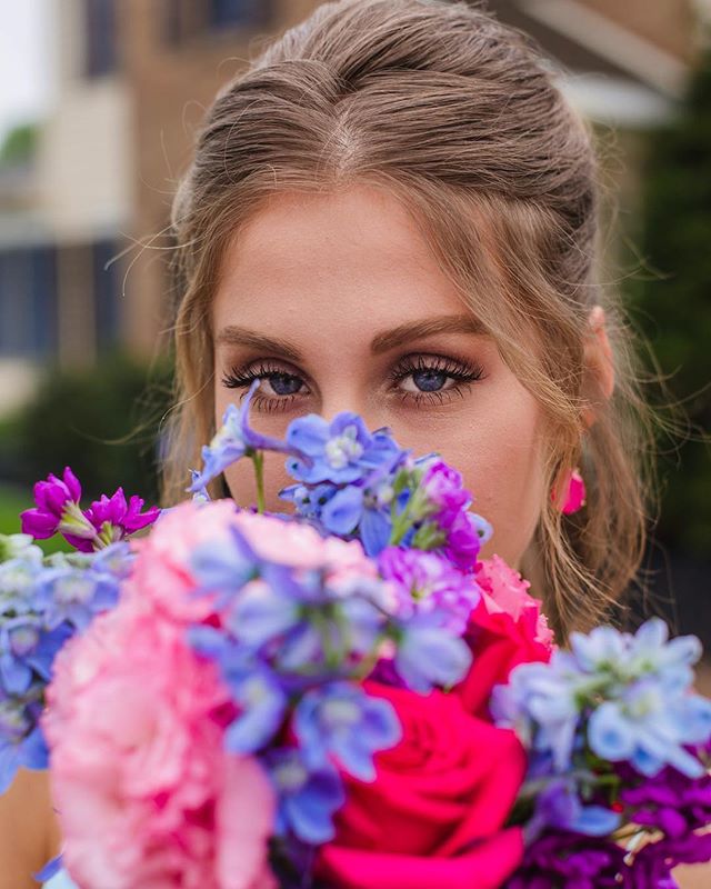 A woman's face is partially hidden behind a vibrant bouquet of pink and blue flowers.