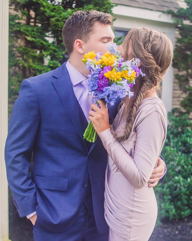 A loving couple shares an intimate moment, hiding behind a beautiful bouquet in a garden setting.