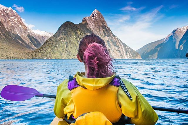 A woman kayaking on a lake surrounded by mountains on a clear day, enjoying the natural beauty.