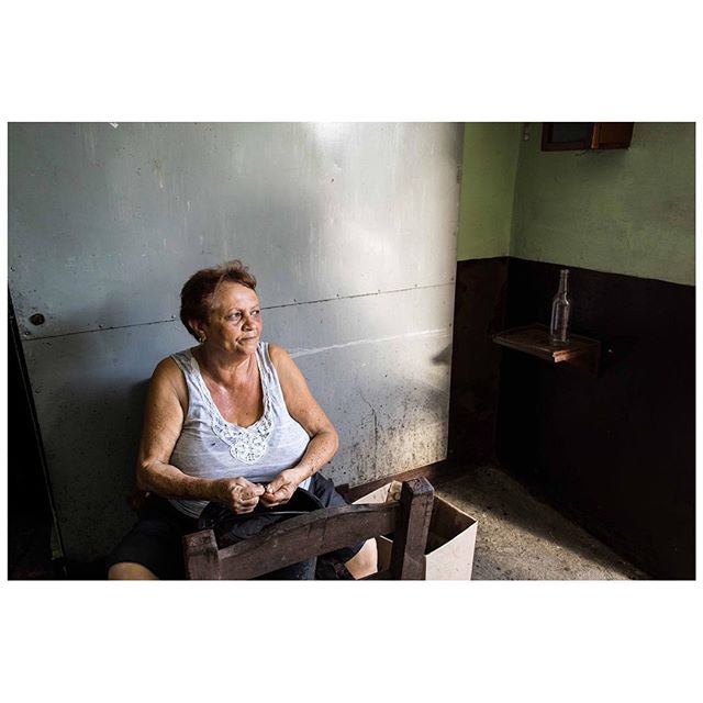 A woman sits quietly on a chair indoors, her expression thoughtful, in a candid, medium shot.