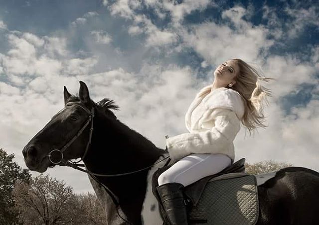 A woman in white riding a black and white horse under a cloudy sky, exuding elegance and freedom.