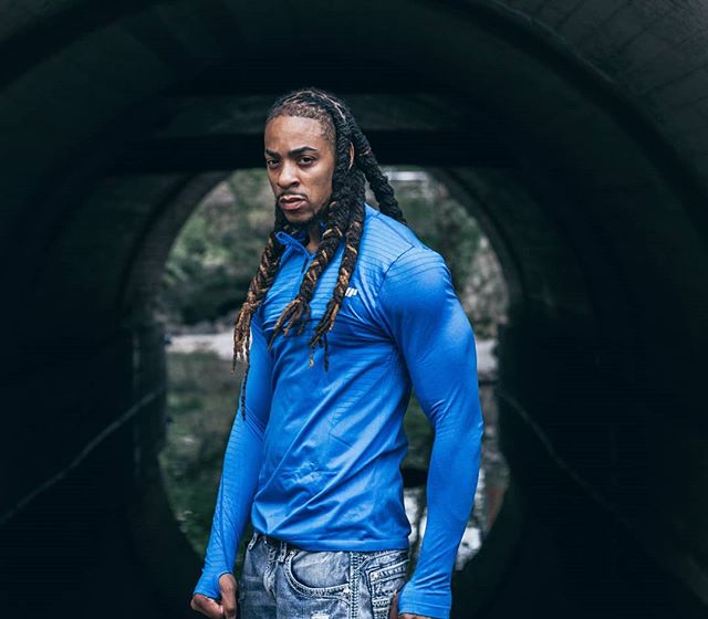 A muscular man with dreadlocks stands confidently in a tunnel, showcasing fitness and determination.