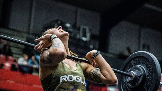 A muscular woman intensely lifts a barbell overhead in a weightlifting competition, showcasing strength and determination.