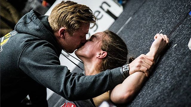 A couple shares a kiss at a climbing gym, showcasing a tender and intimate moment after a climb.
