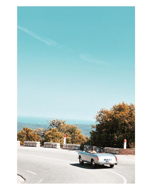 Vintage car driving on a coastal road with scenic views, perfect for a summer getaway.