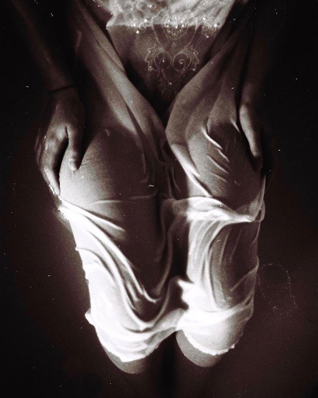 A woman's wet back is illuminated in a close-up studio shot, showcasing an artistic and sensual vintage aesthetic.