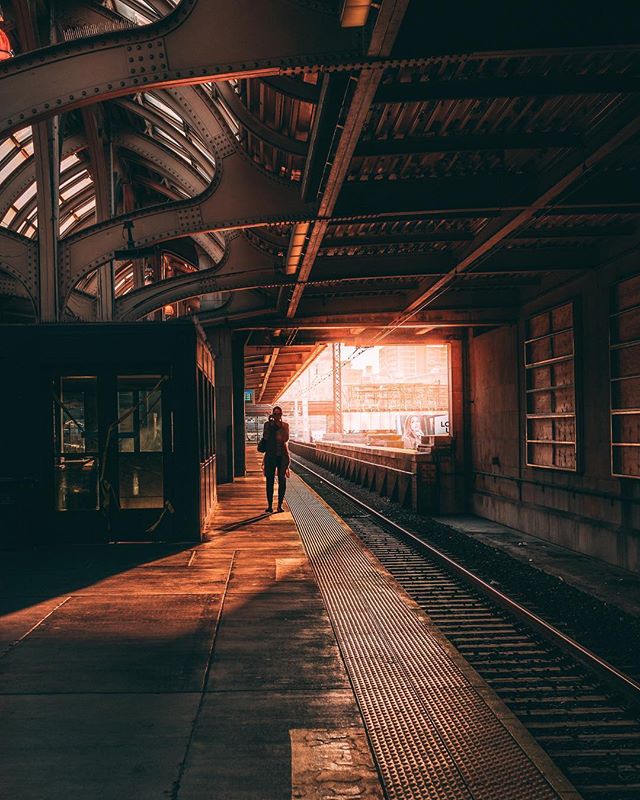 Person walks on train tracks in a gritty urban station at sunset.