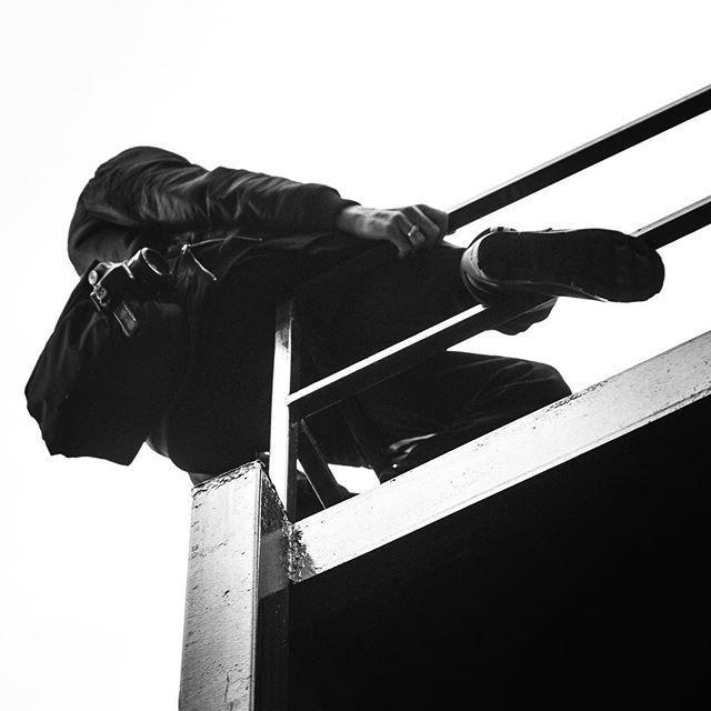 A low-angle shot captures a person climbing a metal structure against a bright sky.