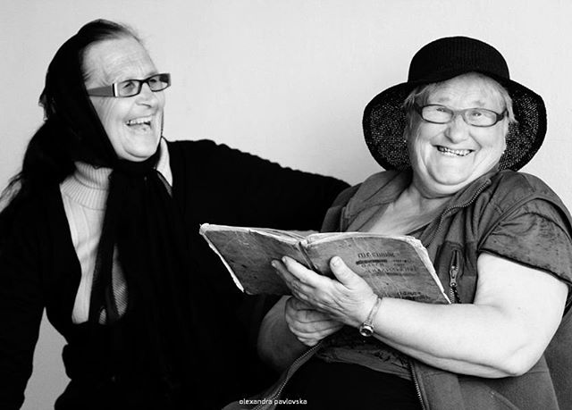 Two elderly women share a laugh over a book, capturing a moment of joy and connection.