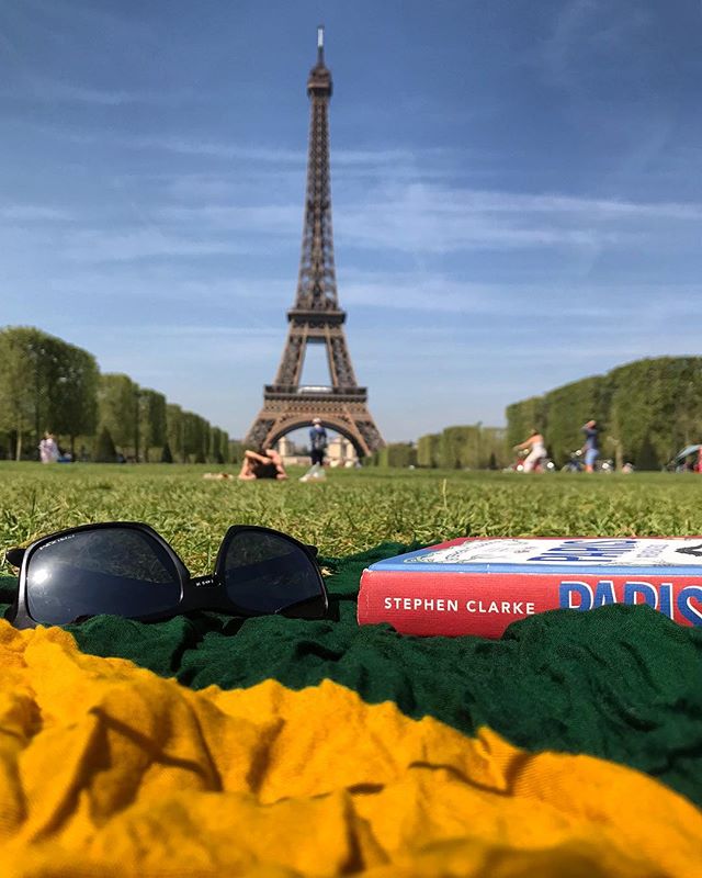 A relaxing picnic with a view of the Eiffel Tower, featuring sunglasses and a book on a blanket.
