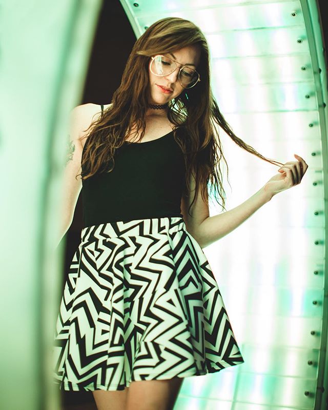 A young woman poses in a patterned skirt and tank top with neon lighting for a modern editorial look.