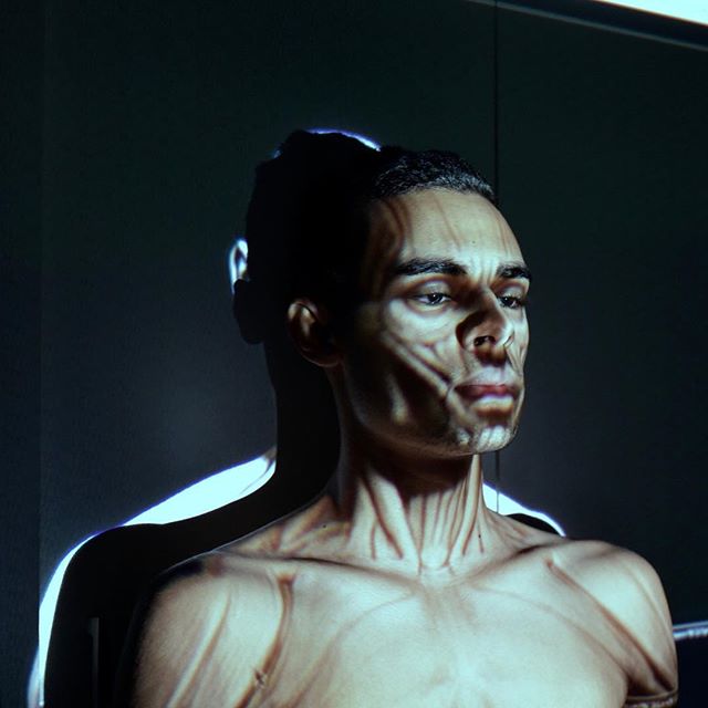 Artistic studio portrait of a man with shadows and light patterns creating a dramatic and conceptual image.