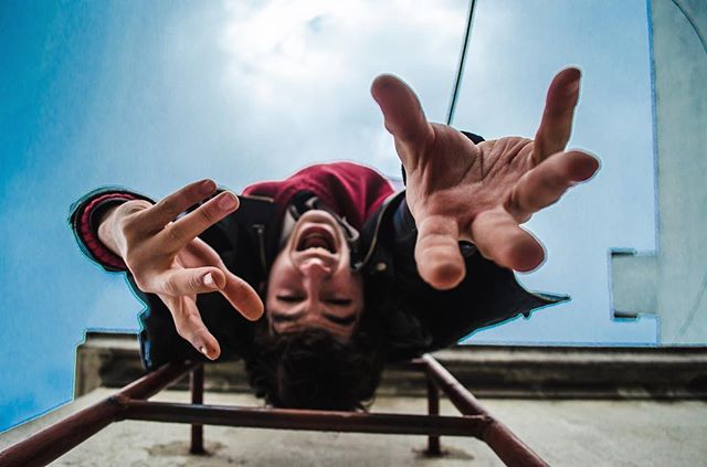 Young man hanging upside down from a ladder reaching towards the camera with a playful expression.