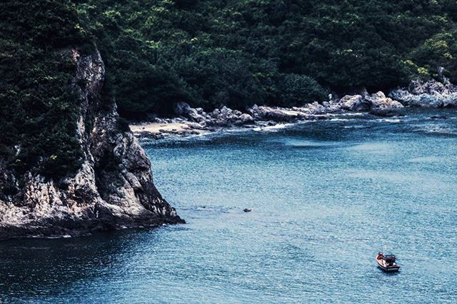 A tranquil coastal scene with a small boat in a blue bay, surrounded by cliffs and lush greenery.