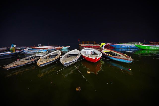 Boats rest on the water at night, illuminated by ambient light. A single person stands by one of the boats.