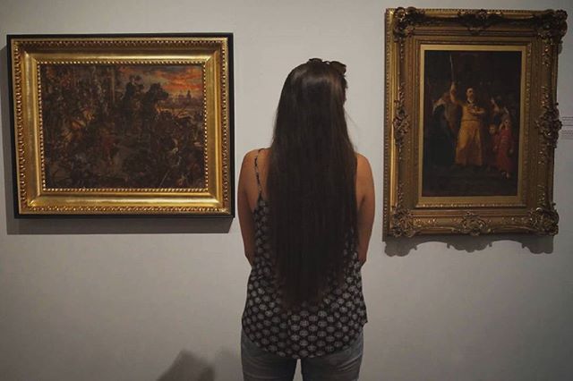 A woman views framed artworks in a museum gallery setting.