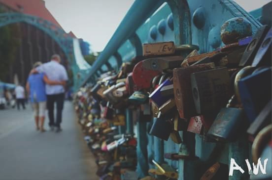 A couple walks arm in arm on a bridge adorned with love locks, symbolizing their bond and commitment.