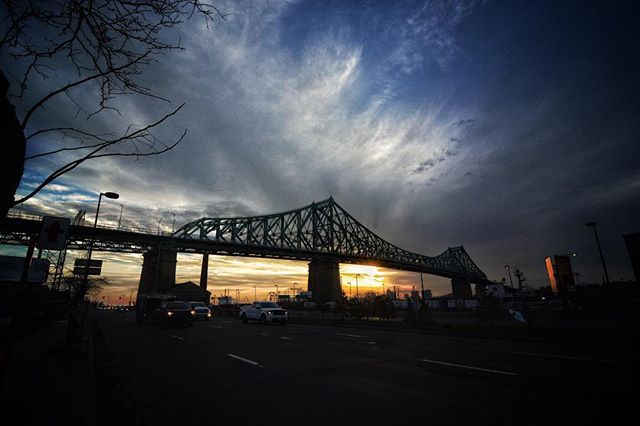 A bridge stretches across a city at dusk, with car lights blurring through the dark street below and a dramatic sky above.