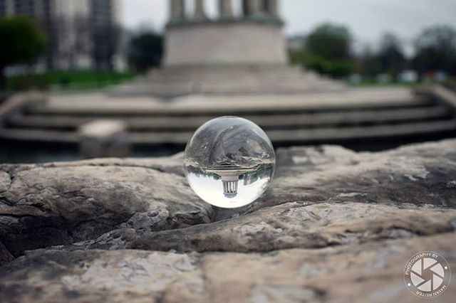 A lensball reflects a monument in a park setting, creating a calm and artistic scene.