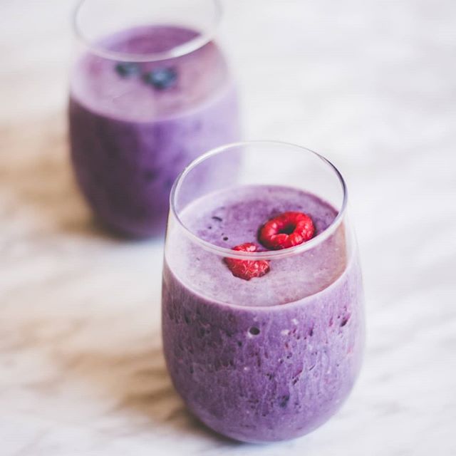Two glasses with purple smoothie topped with berries on a bright surface.