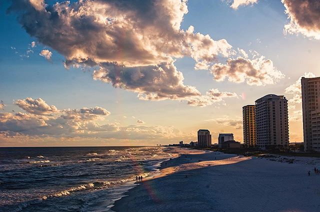 Scenic view of a beach with buildings in the background under a cloudy sky at sunset.