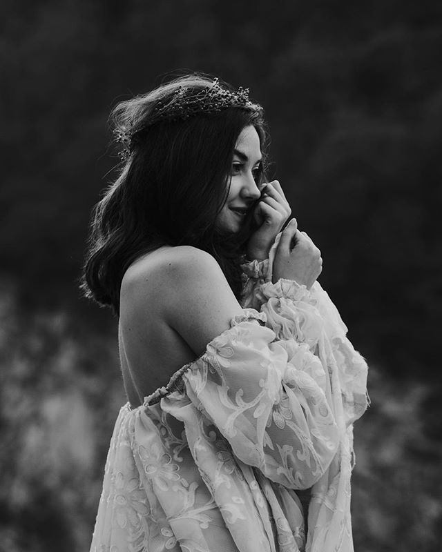 A woman in a vintage dress and flower crown gazes softly in this black and white outdoor portrait.