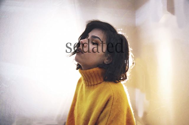 A young woman with short hair wearing a yellow turtleneck sweater is looking up with soft, warm lighting.