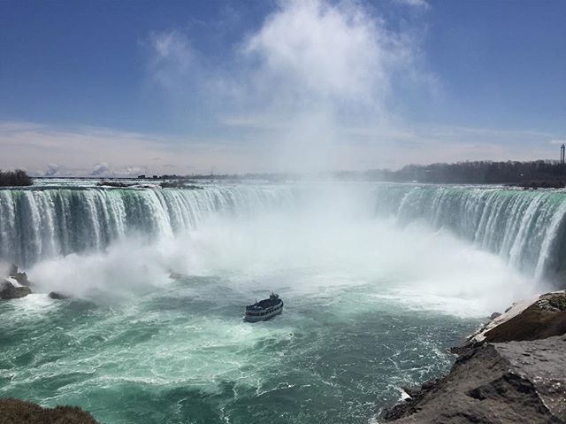 Niagara Falls roars with a boat in the river and blue sky above. A beautiful tourist destination.