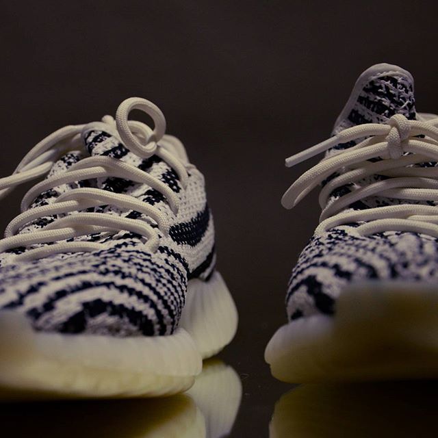A pair of Adidas Yeezy Zebra sneakers are showcased in a close-up studio shot emphasizing the modern design.