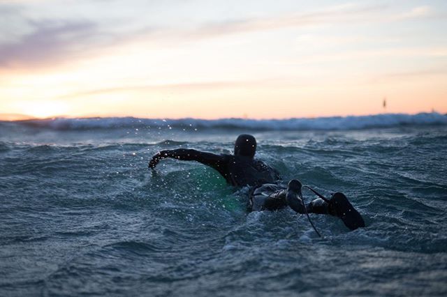 A surfer paddles out on his board in the ocean against a sunset sky. Ideal for fitness and travel themes.