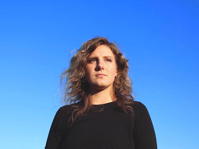 Woman with curly hair looks upwards in portrait against a clear blue sky.