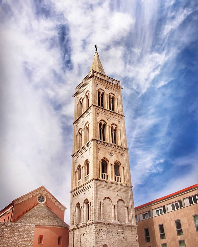 A tall bell tower rises against a partly cloudy blue sky, blending classic architecture with the cityscape.