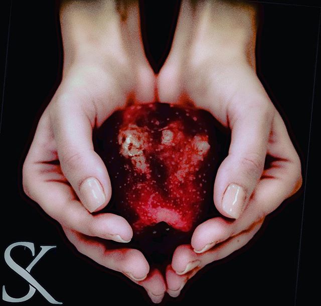 A pair of hands gently cradles a vibrant red apple, against a dark backdrop, creating a sense of mystery.