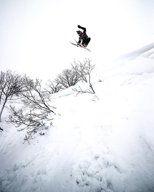 A snowboarder catches air against a snowy mountain backdrop, showcasing extreme winter sports.