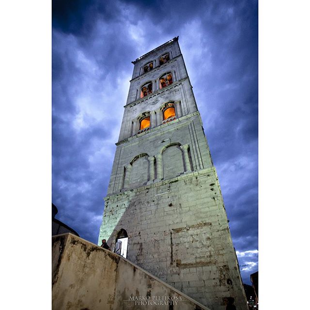 A tall bell tower under a dramatic sky, showcasing historical architecture in an urban setting. 