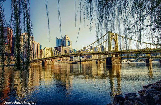 A scenic view of Pittsburgh's bridges and skyline reflected in the river on a calm day.
