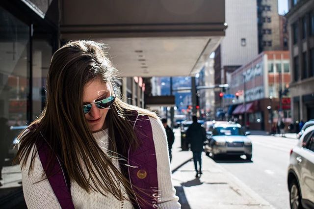 A woman in sunglasses walks along a city street on a sunny day, captured in a candid moment.