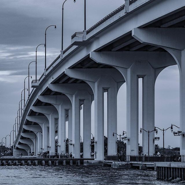 A low angle shot of a large, modern bridge with many supporting pillars over water under a cloudy sky.